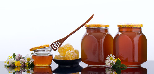 Composition with tasty natural honey in glass jars, honeycomb on black bowl, wooden paddle with...