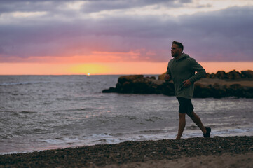 Full body young strong sporty athletic toned fit sportsman man he wearing sports clothes run jogging warm up training at sunrise sun dawn over sea sand beach outdoor on seaside in summer day morning .