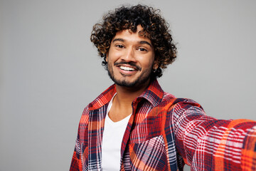 Obraz premium Close up young happy smiling cool Indian man he wearing red shirt casual clothes doing selfie shot pov on mobile cell phone isolated on plain grey color background studio portrait. Lifestyle concept.