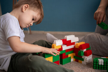 Loving mother and little son playing together on floor, building house from toy construction blocks, enjoying leisure and playtime. Motherhood and childhood