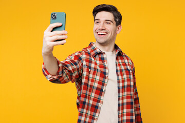 Young smiling happy man he wears red checkered shirt casual clothes doing selfie shot on mobile cell phone post photo on social network isolated on plain yellow orange background. Lifestyle concept.