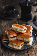 Sweet bun with poppy seed on plate on wooden table.