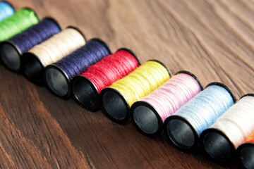 Row of colorful threads on spools are arranged on a wooden surface. Sewing equipment objects