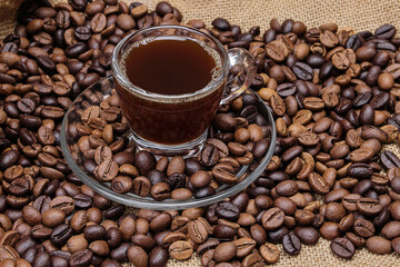 Dark brown Coffee bean macro closeup flow move fall drop pan roll smoking roasting cooking transparent clear glass cup saucer pour liquid on jute fabric background