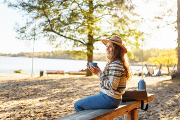 Smiling young woman sits in forest, drinking cups of tea. Enjoy travel, vacation and hot coffee outdoors. Hiking lifestyle, adventure and tourism, rest, relax.