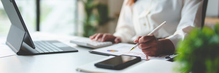 Business concept of Asian businesswoman holding pen and looking at notebook to analyze financial data and make account analysis report. real estate investment information financial system concept