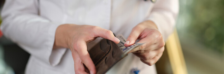 Female doctor putting cash banknotes in wallet