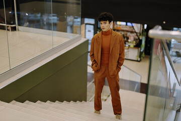 Stylish young man in a brown suit stands on stairs in a modern interior