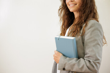 Teacher or young businesswoman has her agenda in her hands. She is going to present the work organization in front of her team. She smiles at the camera. Copy space. Close up.