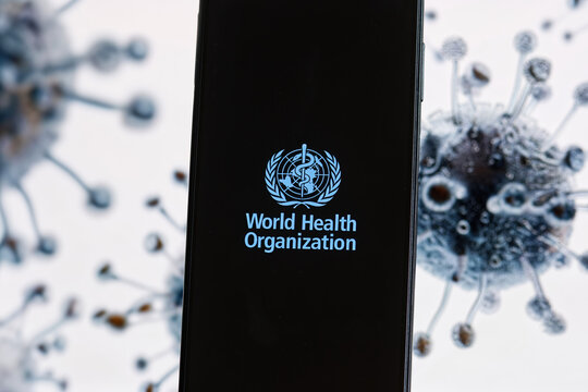 The World Health Organization (WHO) logo displayed on a smartphone screen, with a virus image shown on a computer screen, concept of an epidemic threat.