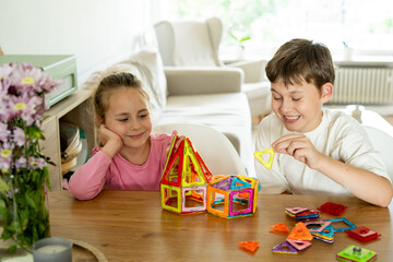 Fototapeta premium Cute children, brother and sister, assemble magnetic constructor at home at the table. Educational games for children. happy