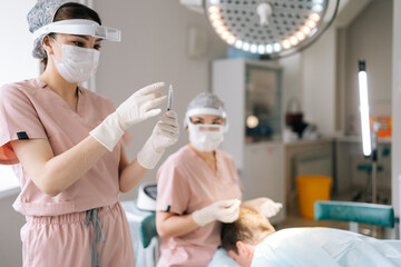 Portrait of gloved female nurse prepares filled syringe by tapping syringe and giving to doctor for...