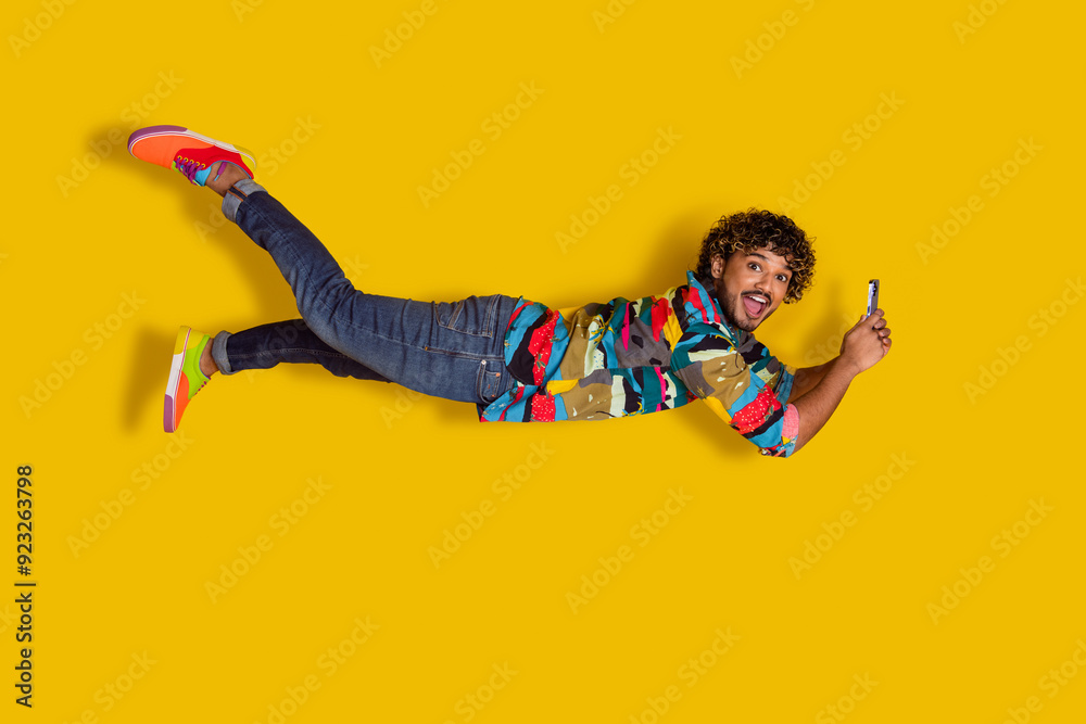 Sticker Full length photo of handsome young male flying hold gadget dressed stylish colorful garment isolated on yellow color background