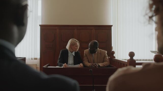 Over the shoulder view of Black male complainant and Caucasian female prosecutor discussing points of case at court session