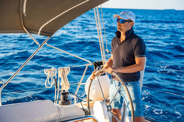 Young man captain stands at the helm and controls a sailboat during a journey by sea