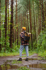 Naklejka premium Woman wearing a yellow beanie and plaid shirt hikes through a wet forest path, carrying a backpack, and enjoying a rainy outdoor adventure. 