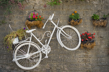 Fototapeta premium A white bicycle hanging in Gjirokastra on the wall while pots with colourful flowers are framing it