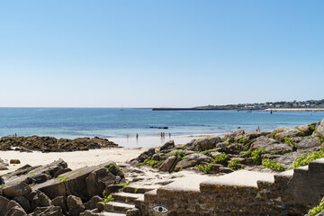 Fototapeta premium Journée estivale sur la plage de Trescadec à Audierne, en Bretagne, où d'énormes rochers dominent le premier plan et les vacanciers profitent du soleil et de la chaleur.