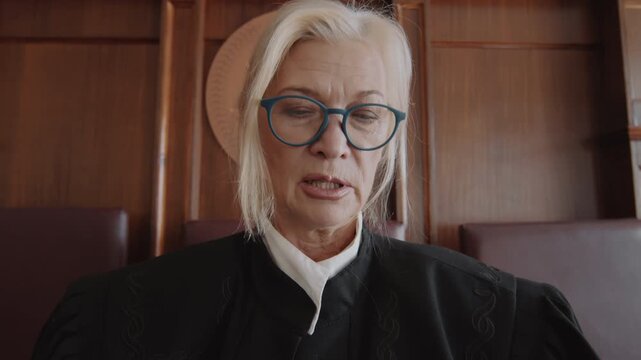 Zoom in shot of senior blond female judge holding folder and reading out verdict after court trial