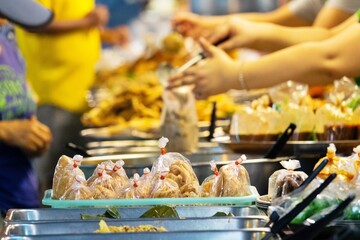 A group of people are standing around a buffet table with plastic bags of food. The bags are filled with various types of food, including sandwiches and other dishes. Concept of community and sharing