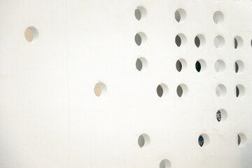A white wall with many small holes in it. The holes are arranged in a grid pattern, creating a unique and interesting texture. Scene is somewhat abstract and minimalist