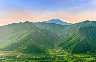 Obraz premium amazing view at a green landscape between two mountains with a high peak with snow and blue cloudy sky on background