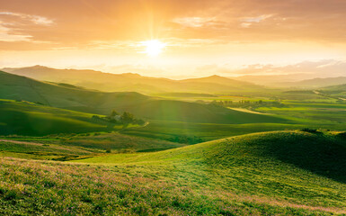 spring season green landscape of green field and meadow in a hill countryside with mountains and beautiful sunset sky on background