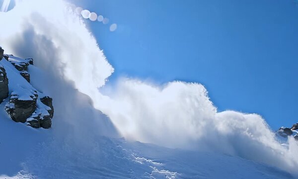 Impressive view of an avalanche falling from a white mountainside, with a sky in shades of blue in the background. The powerful cascade of snow highlights the dramatic effect of the force of nature.