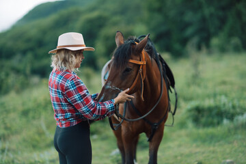 Happy blonde with horse in forest. Woman and a horse walking through the field during the day. Dressed in a plaid shirt and black leggings.