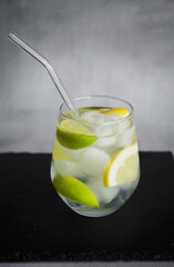 Glass with soda, ice, mint, lemon and lime slices on a black tray on a gray background