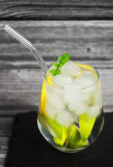 Glass with soda, ice, lemon and lime slices on a black tray on a gray wooden background