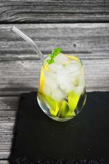 Glass with soda, ice, lemon and lime slices on a black tray on a gray wooden background