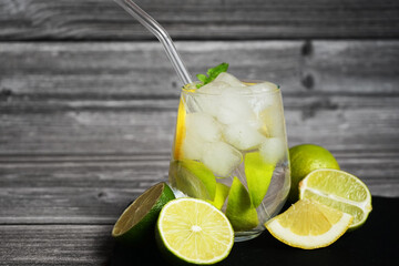 Fototapeta premium Glass with soda, ice, lemon and lime slices next to cut citrus fruits on a black tray on a gray wooden background