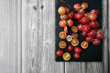 A bunch of large pink grapes next to cut grapes on a black tray on a gray wooden background