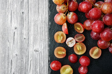 A bunch of large pink grapes next to cut grapes on a black tray on a gray wooden background