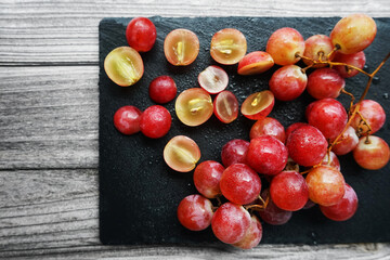 A bunch of large pink grapes next to cut grapes on a black tray on a gray wooden background