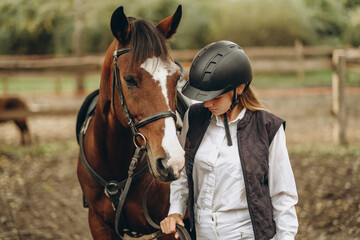 A young female equestrian stands near her horse and prepares for a competition.
