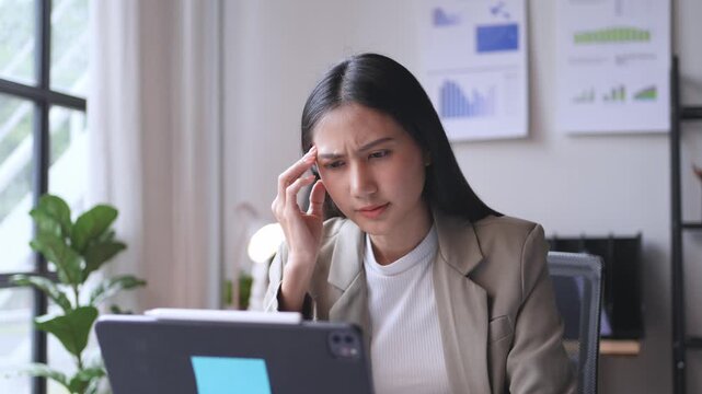 Professional businesswoman shows frustration while working on her laptop in a contemporary office with charts on the wall and houseplants