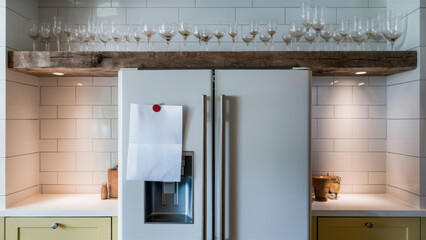 A white refrigerator with a wooden shelf above it and wine glasses on the counter, AI