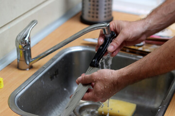 Man washes a knife in kitchen sink 