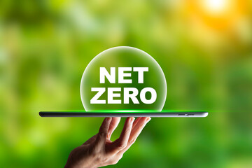 Hand holding tablet Net Zero text on it. natural garden background, wallpaper for net zero emissions concept, carbon footprint to limit global warming and climate change. earth day ,friendly energy,