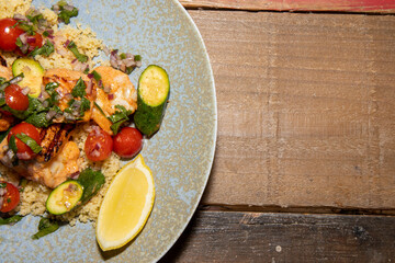 A delicious plate of Spring Salmon and Prawns Skewers with couscous salad and citrus salsa on a wooden kitchen table
