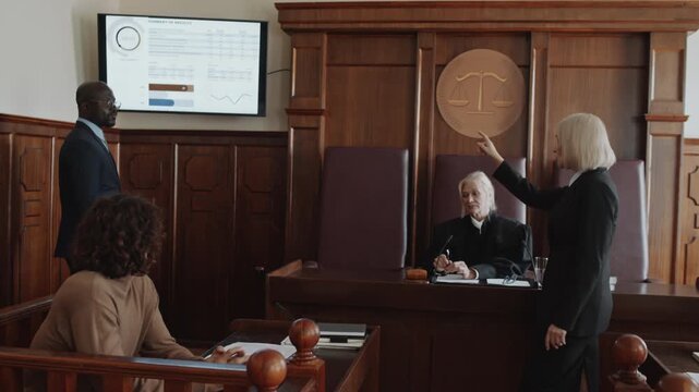 African American male attorney making presentation while defending his young client in courtroom, Caucasian female prosecutor pointing at tv screen and disagreeing