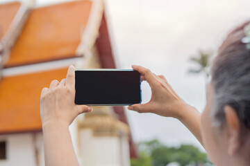 Female photographer with smartphone befor takes a picture of the temple in Thailand.