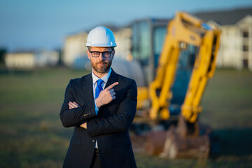 Construction builder investor. Man investor in front of construction site. Successful handsome man standing at modern home building construction. Portrait of midlle aged investor in suit and helmet.