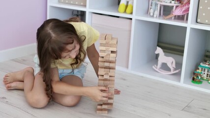 The kid girl is playing board game Jenga in the children's room. The concept of child development. The concept of leisure for children. 4k footage