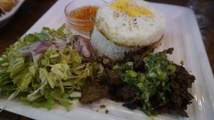 Vietnamese cuisine consisting of rice, fried eggs, vegetable pieces mixed with shallots, a bowl of Vietnamese chili sauce and grilled beef ribs at a Vietnamese restaurant
