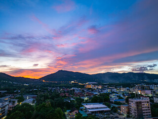 An aerial view of the Phuket islands bathed in soft pastel hues during sunset. The tranquil sea below is dotted with islands, while the sky above is painted with delicate pink and orange clouds.