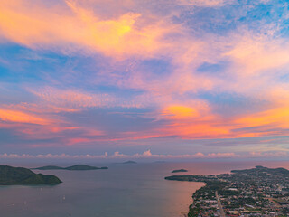 An aerial view of the Phuket islands bathed in soft pastel hues during sunset. The tranquil sea below is dotted with islands, while the sky above is painted with delicate pink and orange clouds.