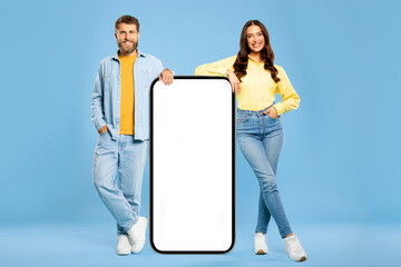 Smiling European man and woman near huge blank smartphone screen, perfect for advertising app,...
